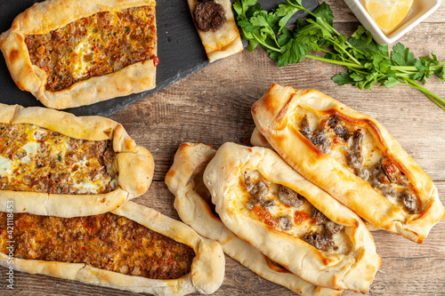 Kasarli sucuklu pide and kiymali pide are traditional Turkish flatbreads similar to pizza with meat and cheese toppings. They are served with lemon and parsley. An assortment of fresh baked on wood.