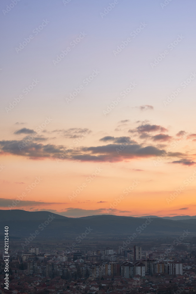 Stunning blue hour view of a city with colorful buildings, burning sky and background horizon mountains