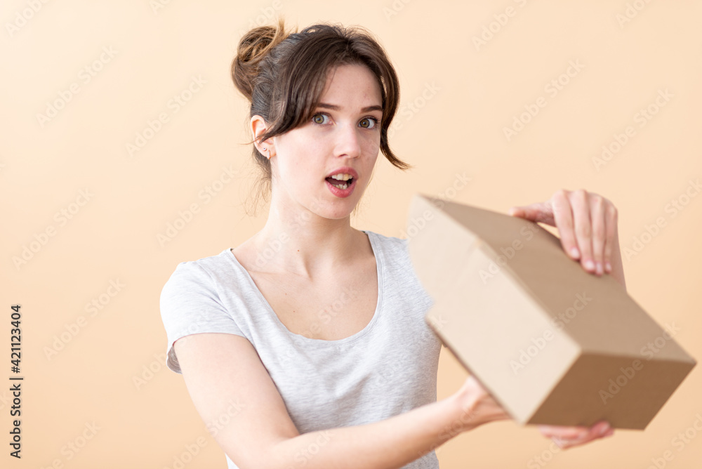 A surprised young girl opens a cardboard box. Online delivery concept. A surprised young girl opens a cardboard box. Online delivery concept.