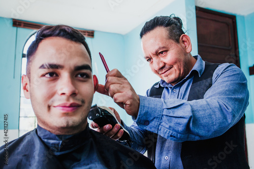 hispanic man stylist cutting hair to a client in a barber shop in Mexico city