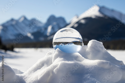 A scenic snow peaked mountain range view inverted inside a lens ball, on a snow bank on a sunny day. photo