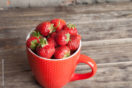 Fresh organic strawberry in red cup on wooden background. Healthy breakfast. Natural farming. Growing fruit. 