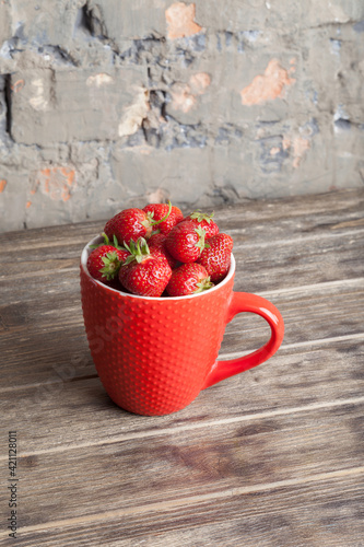 Fresh organic strawberry in red cup on wooden background. Healthy breakfast. Natural farming. Growing fruit. 