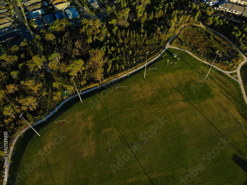 Aerial photograph of suburban sporting field and housing estate at sunset, with blue sky and white clouds.