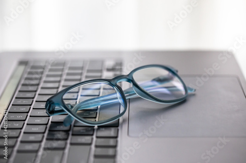 Eyeglasses on laptop keyboard on wooden table. Close up