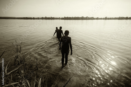 Europe, Ukraine, Kharkov region. Three boys will go to the lake on a warm evening. Glare from the sun on the water.