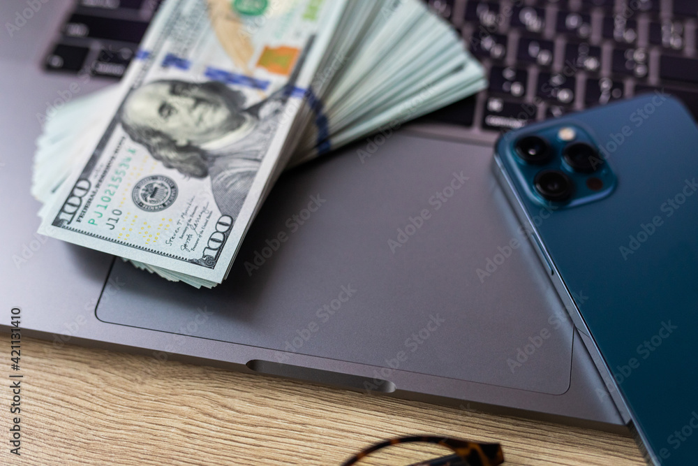 Business concept - laptop, banknotes of us dollars, smart phone and glasses. Top view of the texture of expensive wood. Picture with space for your text. Business concept - laptop, banknotes of us dollars, smart phone and glasses. Top view of the texture of expensive wood. Picture with space for your text.
