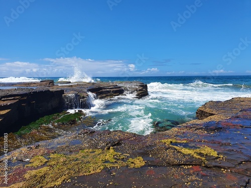 Waves crashing over rocks on sunny blue sky day, Austimere Beach, NSW, Australia