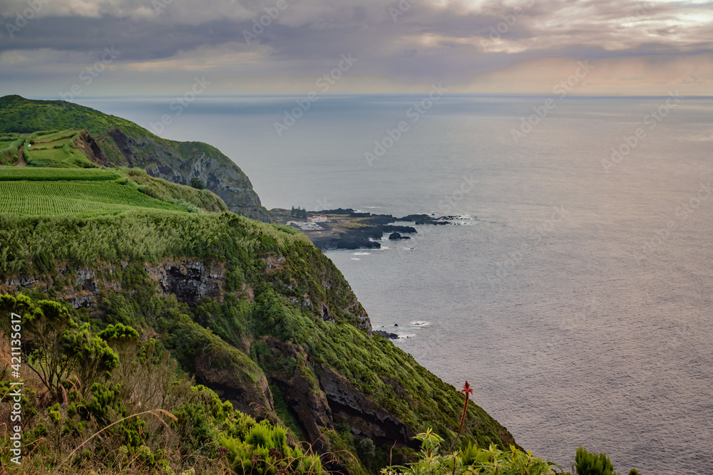 Cliff with vegetation and green field overlooking the hot sea springs of Ponta da Ferraria in lava fajã at sunset, São Miguel - Azores PORTUGAL