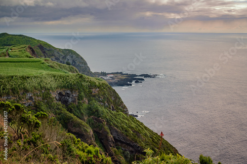Cliff with vegetation and green field overlooking the hot sea springs of Ponta da Ferraria in lava fajã at sunset, São Miguel - Azores PORTUGAL