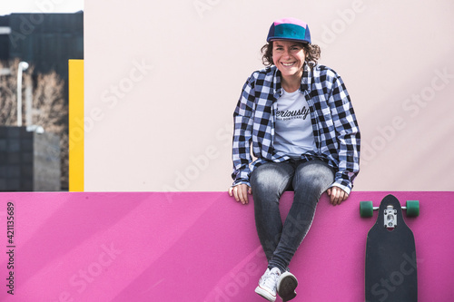brunette woman with cap and skateboard on colorful background © jonarrillaga