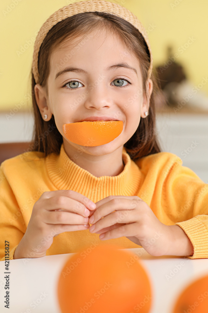 Cute little girl eating orange in kitchen Cute little girl eating orange in kitchen