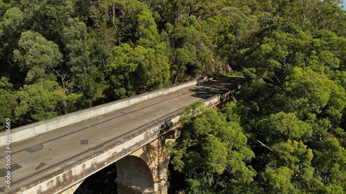 Drone images of the Knapsack Bridge, an old sandstone arch bridge, on a sunny spring morning surrounded by green eucalyptus trees.