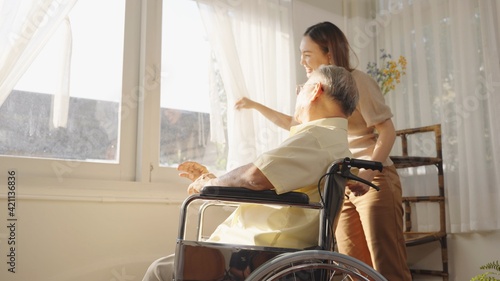Asian elderly father who sitting on wheelchair show her lovely daughter to look at something through window very happy and smile after he survive from Surgery. Caregivers at Home, Healthcare.
