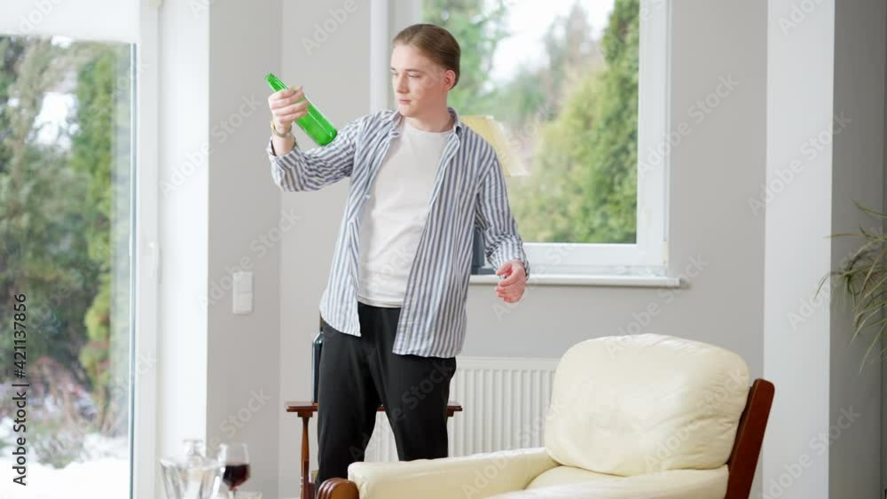 Wide shot portrait of drunk Caucasian young man standing indoors with empty beer bottle. Drunken frustrated guy at home. Alcohol addiction and depression concept. Wide shot portrait of drunk Caucasian young man standing indoors with empty beer bottle. Drunken frustrated guy at home. Alcohol addiction and depression concept.