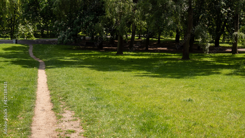 An empty footpath next to a large lawn in a park on a warm sunny day An empty footpath next to a large lawn in a park on a warm sunny day
