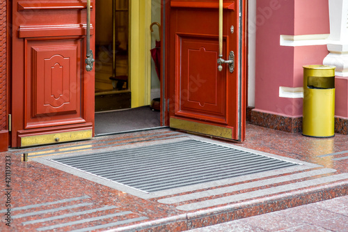 open wooden composite door with glass building entrance with threshold and foot mat and yellow urn of retro european style architecture, nobody.
