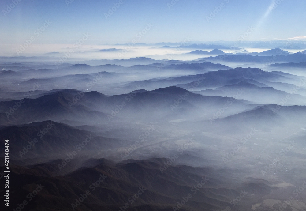 Clouds linger over hills stretching into distance, as photographed from airplane window flying over Chile.