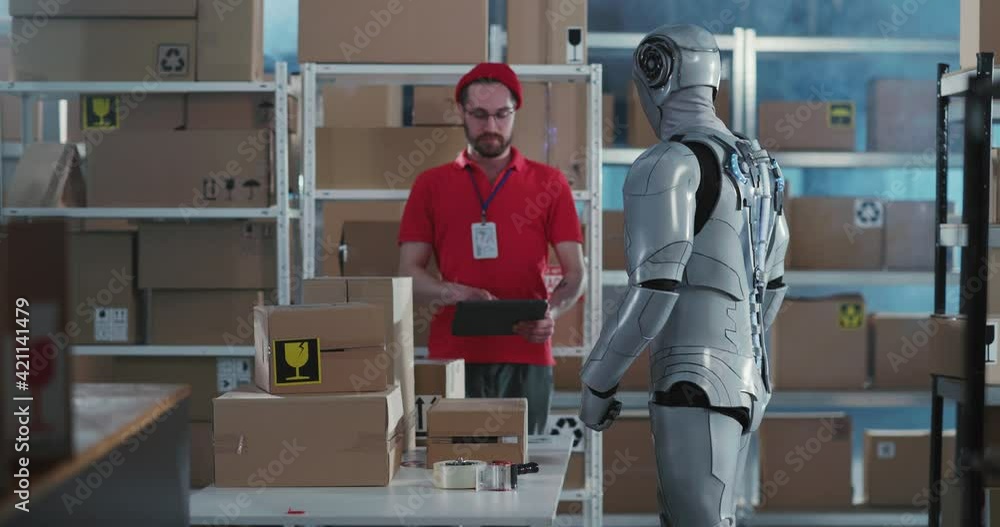 Caucasian post office worker in red uniform cooperating with futuristic worker wearing cybernetic clothes carrying delivery boxes in workshop. Caucasian post office worker in red uniform cooperating with futuristic worker wearing cybernetic clothes carrying delivery boxes in workshop.