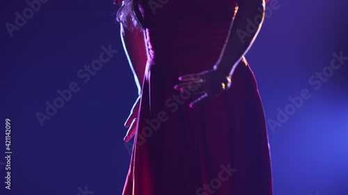 Camera pans over slender body of woman in red dress dancing passionate flamenco. Dancer performs Argentine choreography against the backdrop of dark smoky studio with blue lights. Close up silhouette.