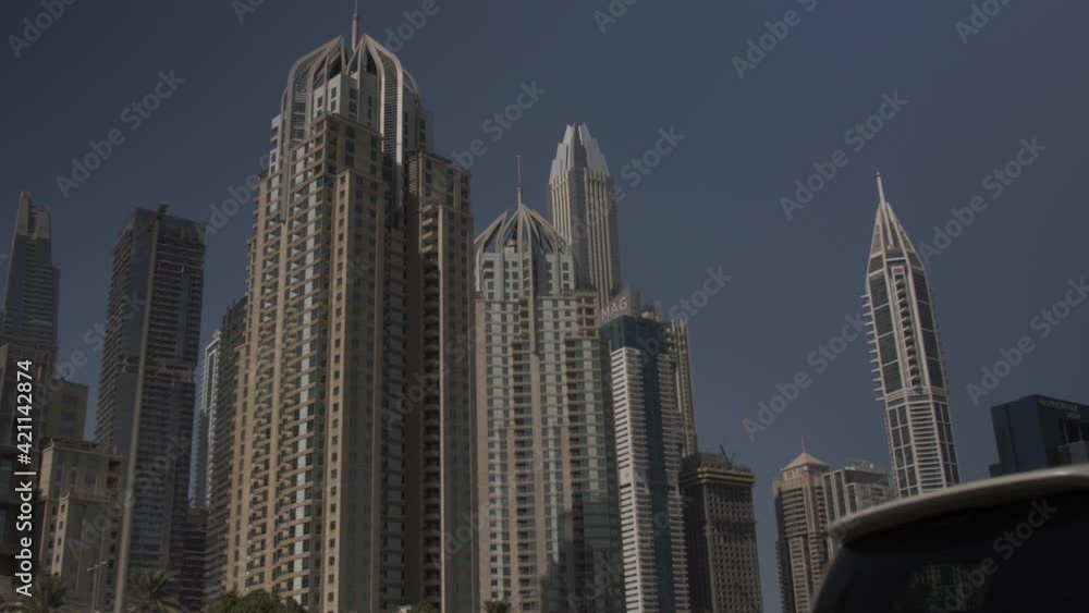 A car drives past tall buildings and skyscrapers in the large city of Dubai in the United Arab Emirates. Filmed in 60fps slow motion. A car drives past tall buildings and skyscrapers in the large city of Dubai in the United Arab Emirates. Filmed in 60fps slow motion.