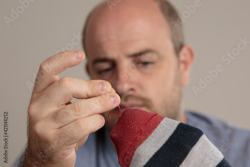 Photography Close-up detail shot of a man sewing a sock by hand, with needle and thread
