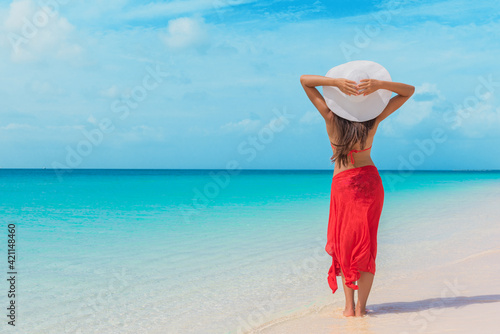 Photos Beach summer vacation free relaxing woman enjoying sun wearing hat and red skirt with arms behind standing at the blue idyllic ocean