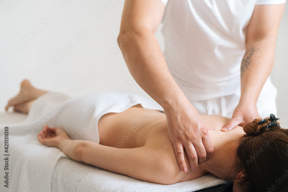Fototapeta premium Male masseur with strong hands professionally massaging scapulas and shoulders to female client. Beautiful naked young woman with perfect skin getting relaxing back massage at spa salon.