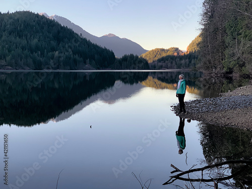 Person on lake shore reflections. Calm mirror like Buntzen lake at sunrise. Port Moody. Grater Vancouver area. British Columbia. Canada