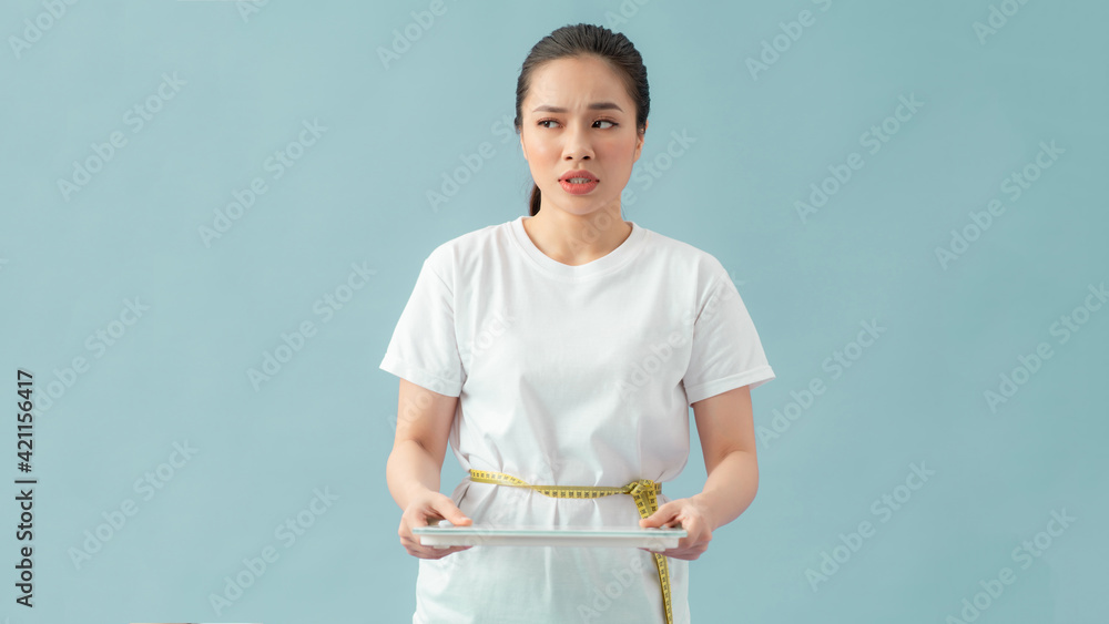 woman measuring waist with tape on knot isolated on blue background, holding scales woman measuring waist with tape on knot isolated on blue background, holding scales