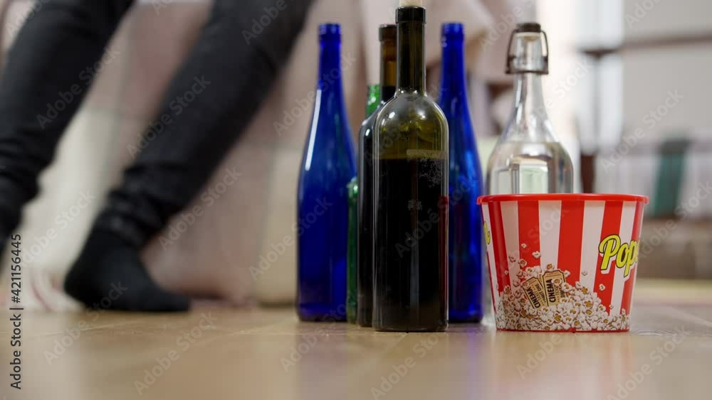 Alcohol bottles and popcorn on floor with legs of drunk man walking to