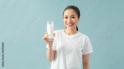 Portrait of a satisfied young asian woman drinking milk from the glass isolated over blue background