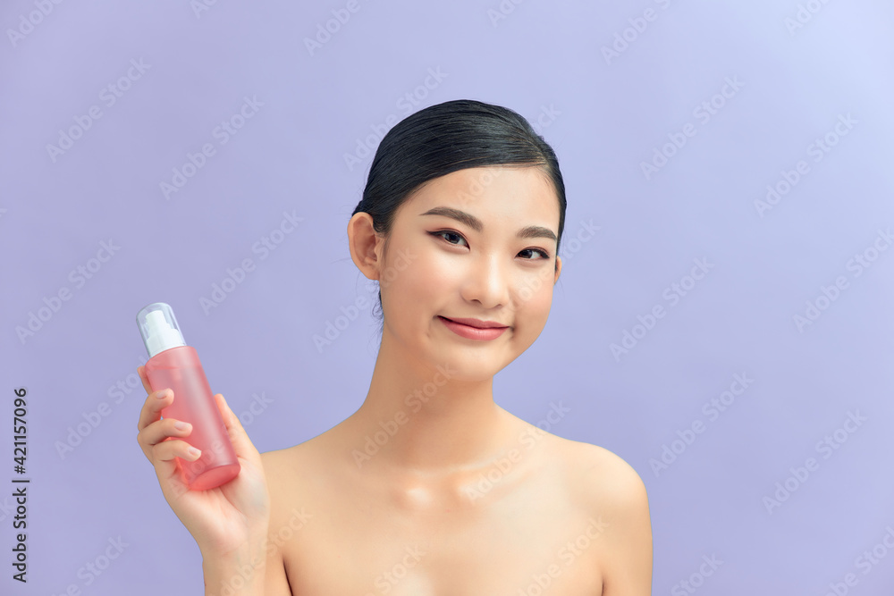 Beauty portrait of an attractive happy healthy topless brunette woman isolated over purple background, showing cosmetic bottle Beauty portrait of an attractive happy healthy topless brunette woman isolated over purple background, showing cosmetic bottle