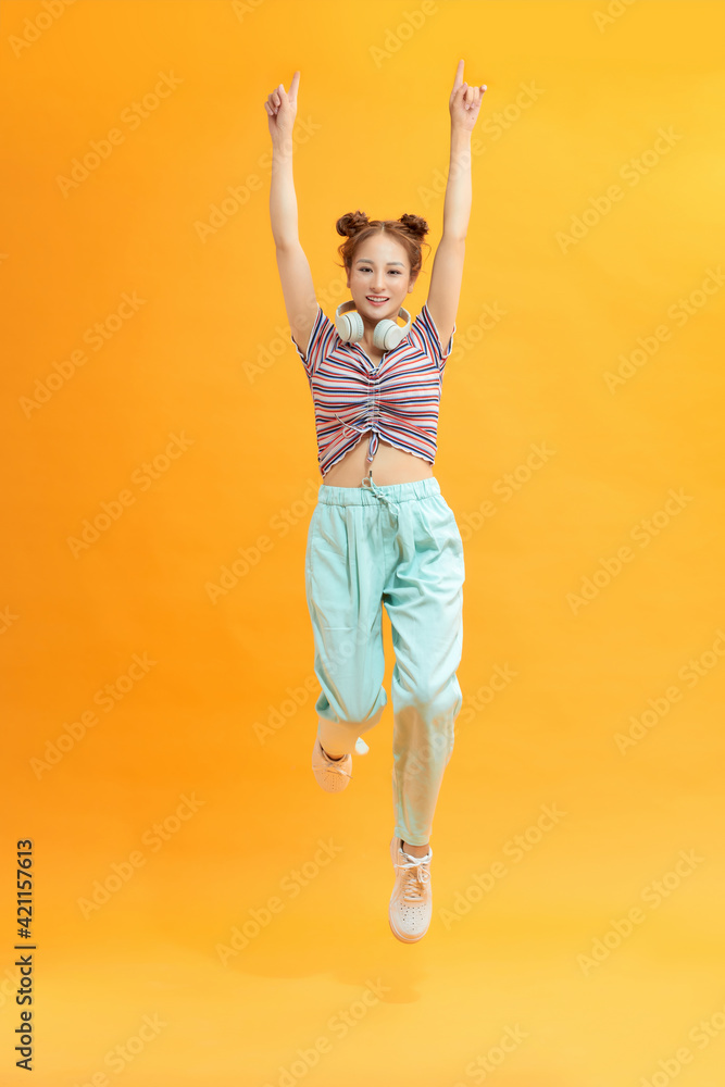 Full length photo of joyful lady jumping high listening modern youngster playlist music through cool earflaps isolated on yellow background Full length photo of joyful lady jumping high listening modern youngster playlist music through cool earflaps isolated on yellow background
