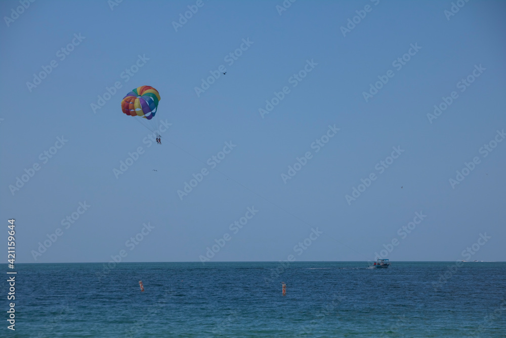 Two people parasailing above blue ocean waters with a boat on the horizon on a sunny summer day with blue skies above. Two people parasailing above blue ocean waters with a boat on the horizon on a sunny summer day with blue skies above.
