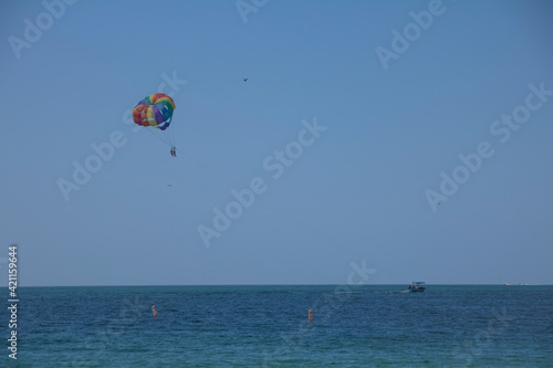 Two people parasailing above blue ocean waters with a boat on the horizon on a sunny summer day with blue skies above.