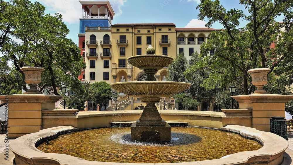 Fototapeta premium Fountain in the city square. Water splashes down the stone bowls. Round pool. Nearby are green trees, a residential building. South Africa. Johannesburg