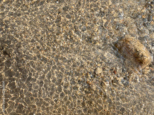 bright daylight shines on a surface of sparkling crystal clear hot spring river with big and small brown rocks and sand beneath it