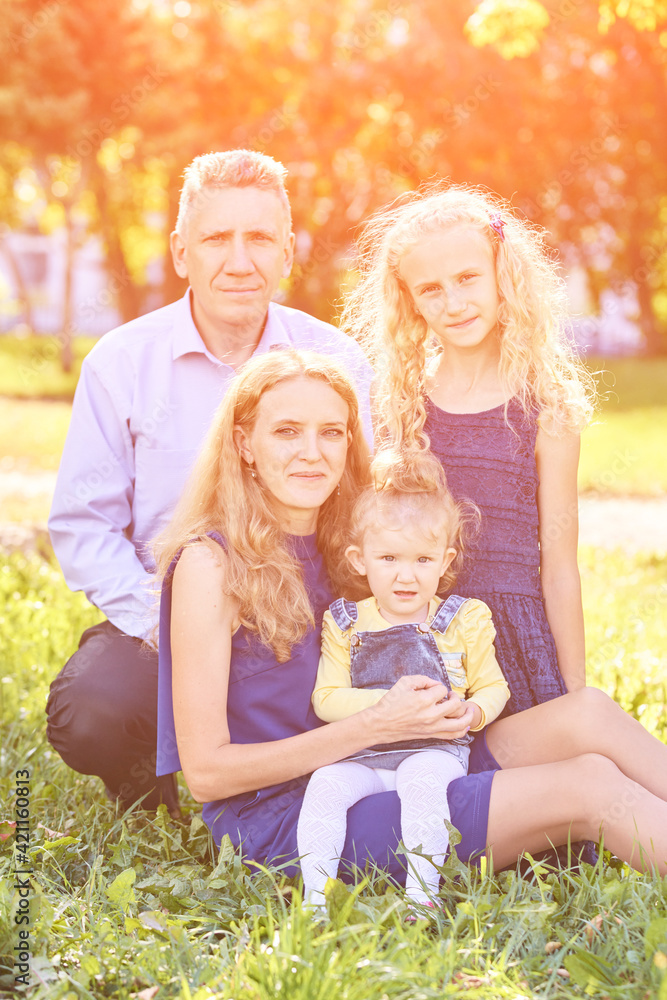 Fototapeta premium Parents with two little daughters at park. Happy family portrait. Nature lifestyle. Summer time. Caucasian people together. Outdoor parenthood
