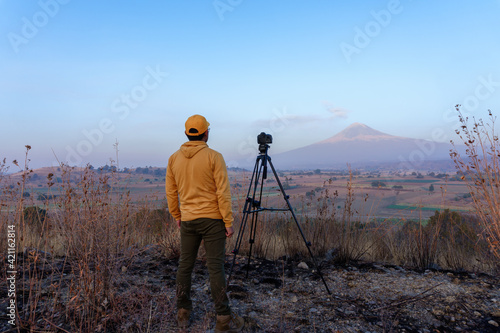 Young Mexican professional photographer with a camera in a field with mountains in the background