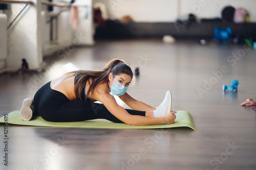 Fototapeta Naklejka Na Ścianę i Meble -  Sporty woman practicing yoga wearing protective mask