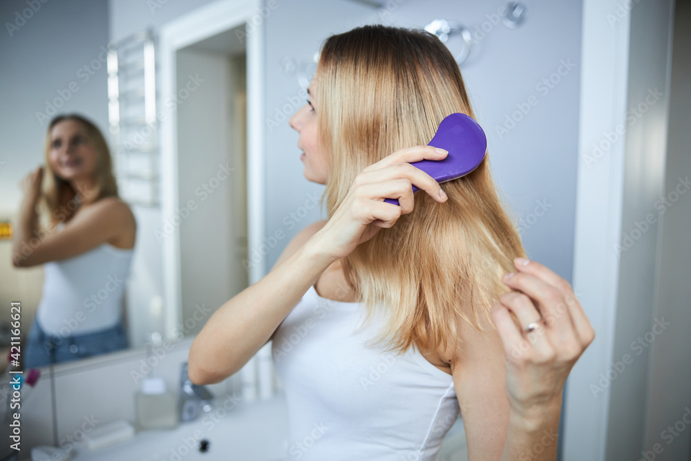 Fototapeta premium Blonde young woman brushing hair at home