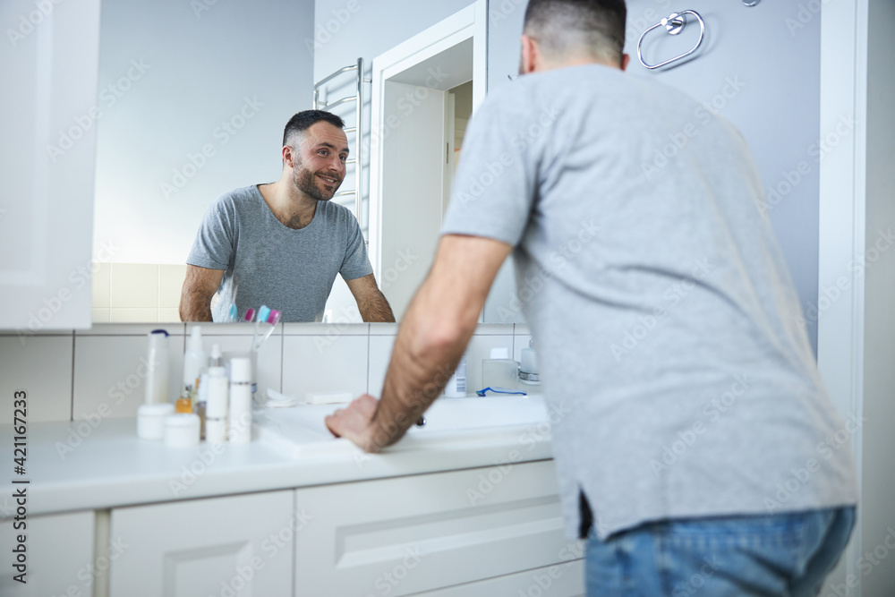 Cheerful young man looking in the mirror in bathroom
