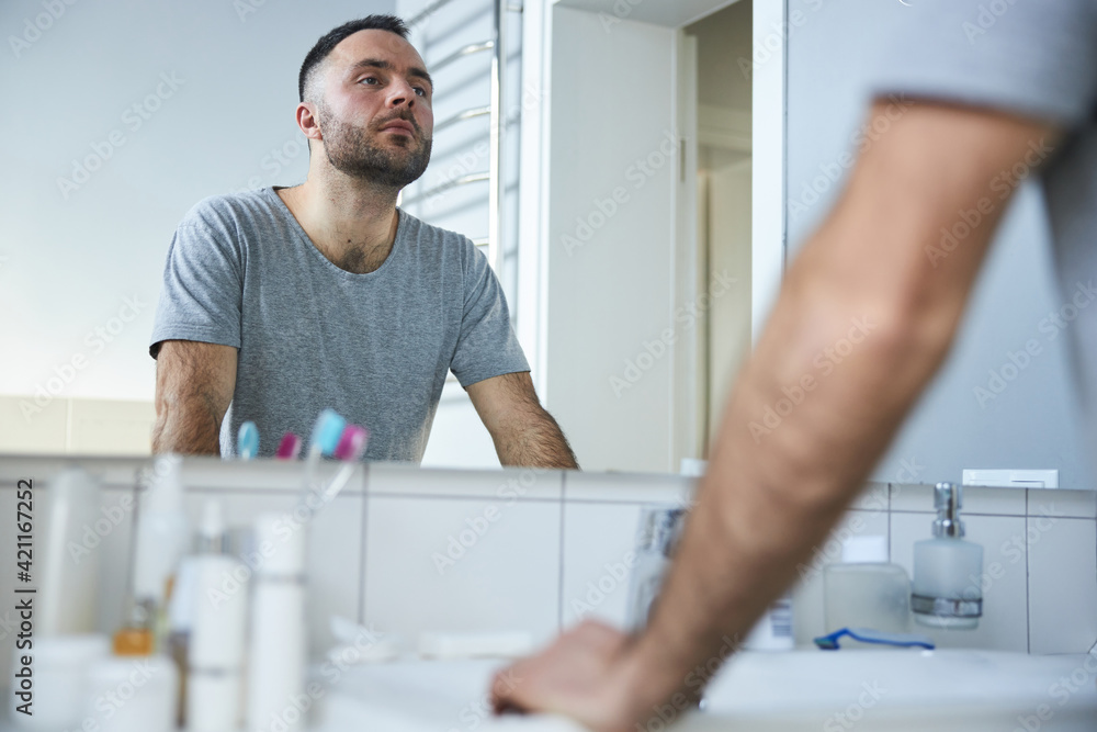 Attractive young man looking in the mirror in bathroom Attractive young man looking in the mirror in bathroom