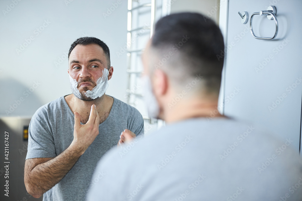 Obraz premium Bearded man applying shaving cream on face in bathroom