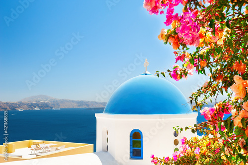 Santorini island, Greece. Traditional greek church with blue dome and tree with pink flowers. Famous travel destination