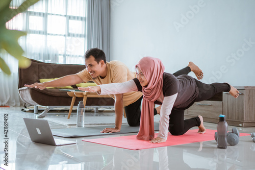 Asian muslim fitness couple stretching and looking at online video tutorial via laptop