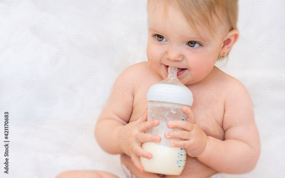 Happy toddler girl drinks milk from a bottle. Baby food. Concept of artificial feed. Happy toddler girl drinks milk from a bottle. Baby food. Concept of artificial feed.