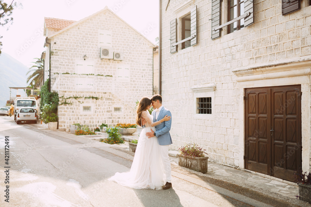 The bride and groom are embracing near the beautiful white houses in the old town of Perast 