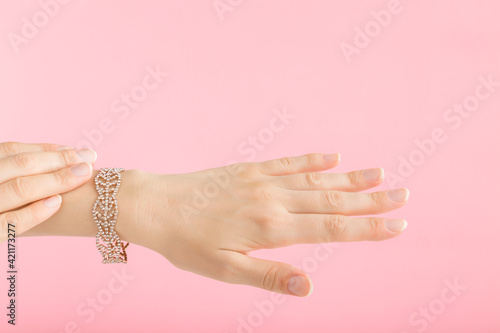 Bracelet of small gems on young adult woman wrist isolated on light pink background. Pastel color. Beautiful groomed hands. Soft touch. Closeup. Side view.